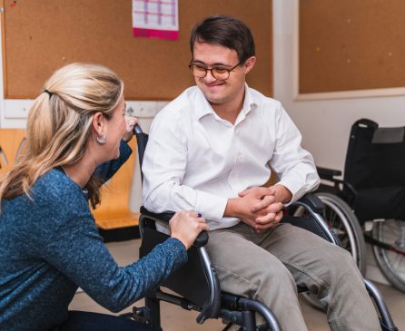 Empathetic Encounter: Woman Connects with Man in Wheelchair with Down Syndrome A heartfelt chat between a woman and a smiling man with Down Syndrome in a wheelchair.
