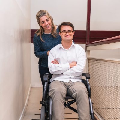 Warm Companionship: Supportive Woman Pushing Man’s Wheelchair A man with Down Syndrome enjoys a companion's push in his wheelchair.